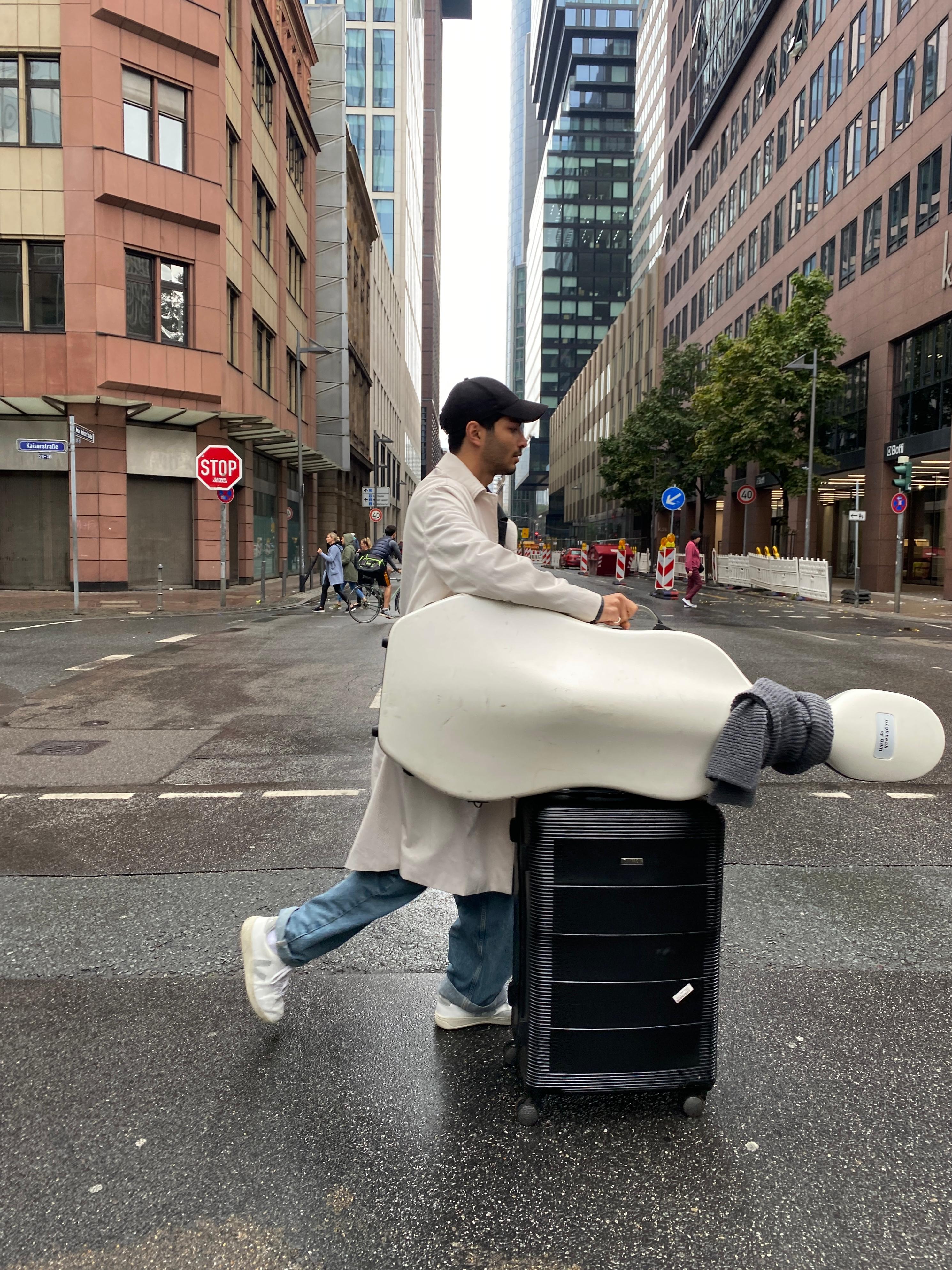 Yunus Altıkanat crossing a Frankfurt street with cello case and suitcase