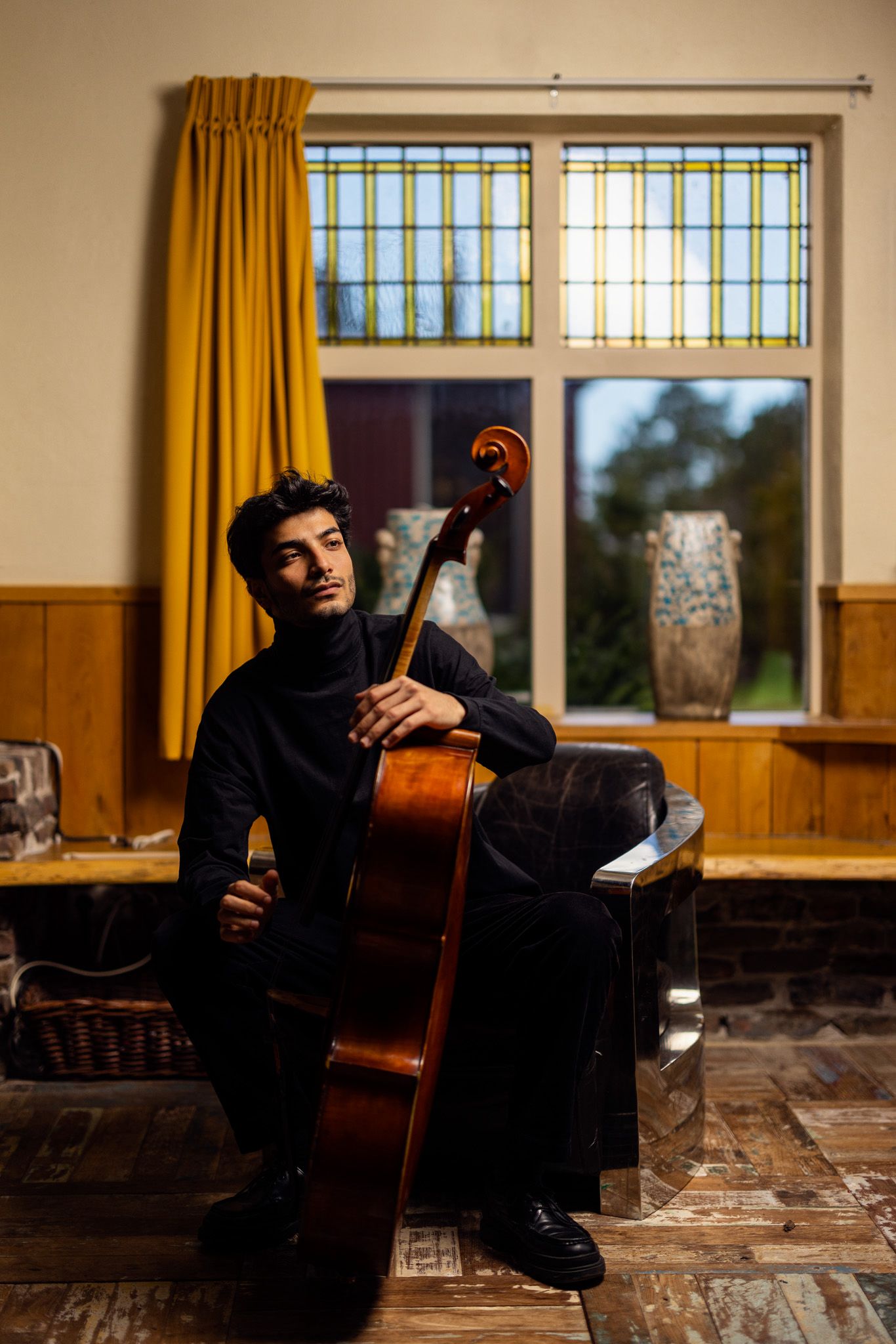 Yunus Altıkanat seated with his cello in front of a stained-glass window